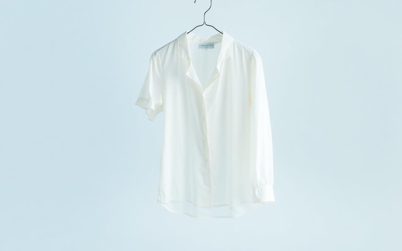 A cream silk blouse hanging against a pale blue background after steam finishing